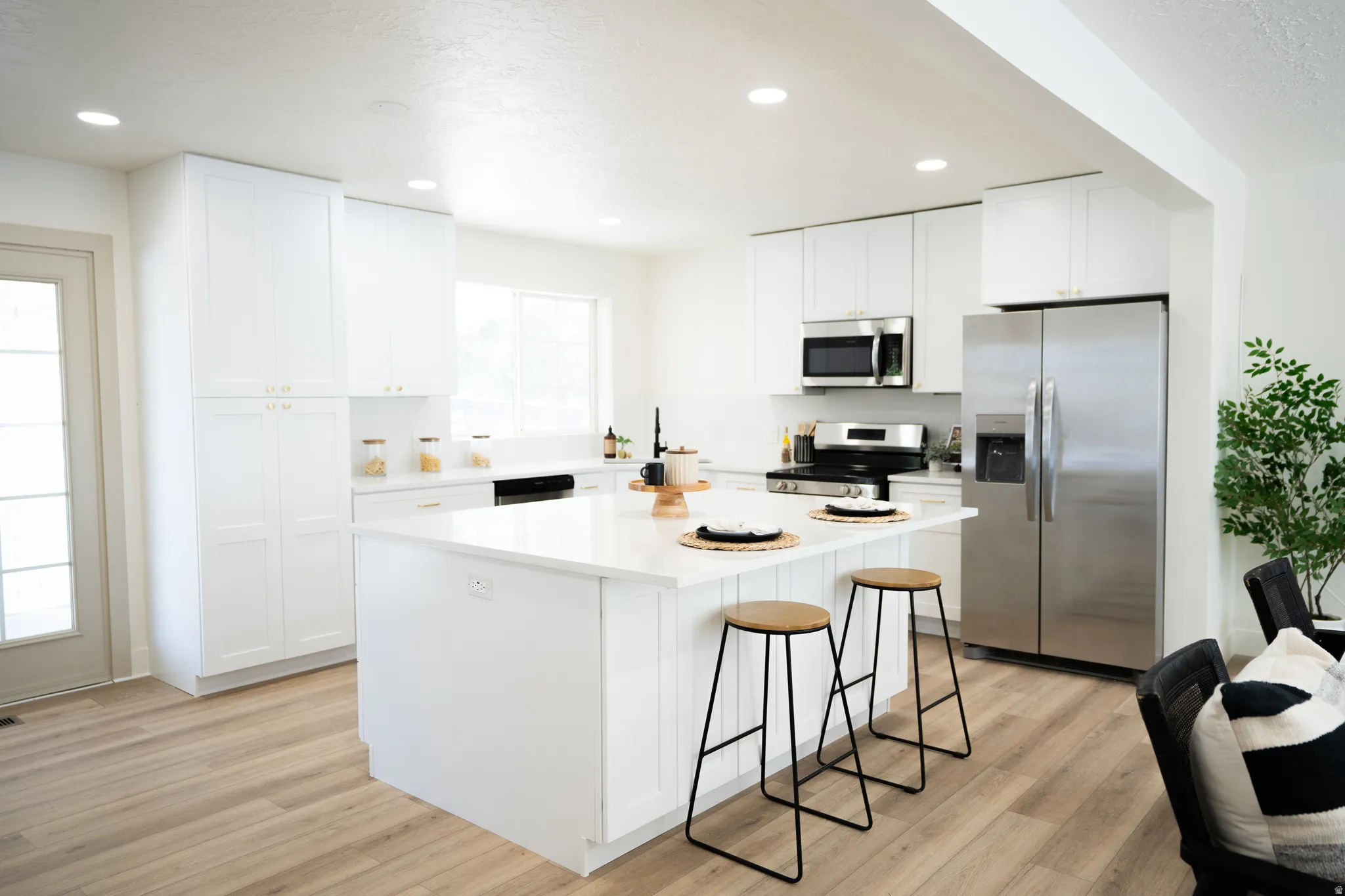Open-concept kitchen featuring a large central island with seating, white cabinetry, stainless steel appliances, and wood-finish flooring