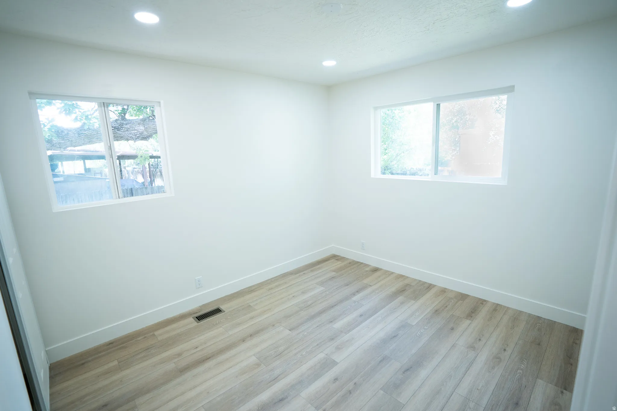 Room featuring wood-finish flooring, two windows, recessed lighting, and white baseboards