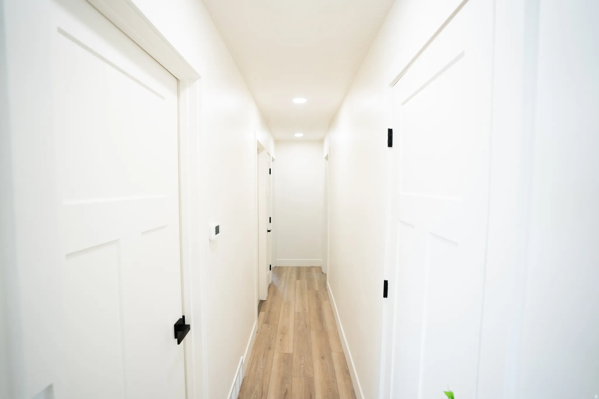 Hallway featuring crisp white walls, wood-finish flooring, recessed lighting, and modern white doors with black hardware