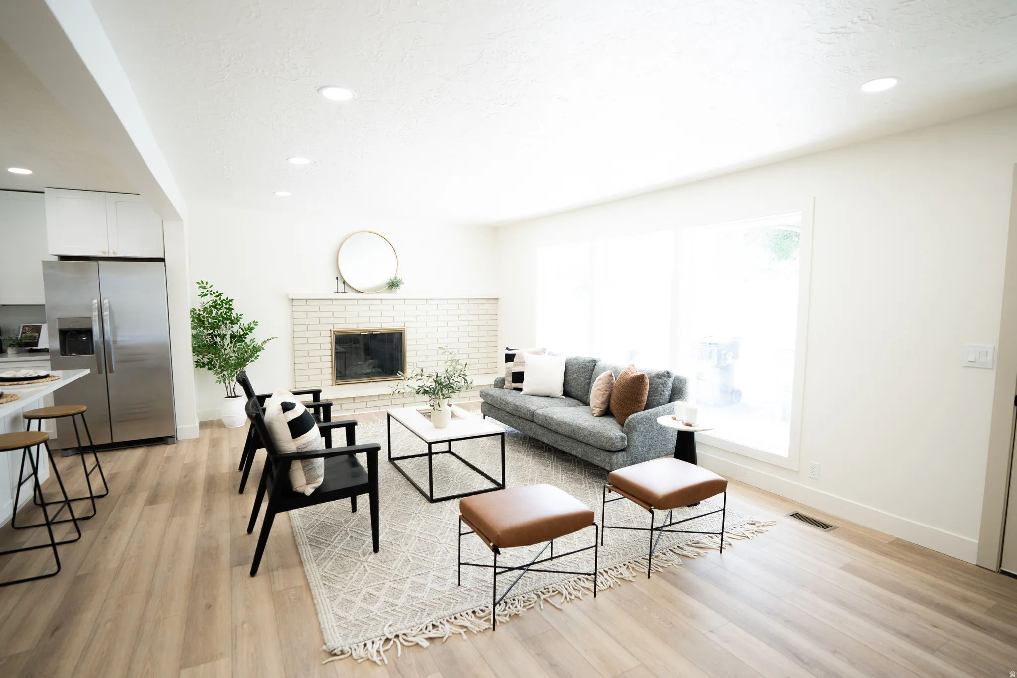 Expansive living area featuring light wood-finish flooring, a white brick fireplace, recessed lighting, and a large picture window