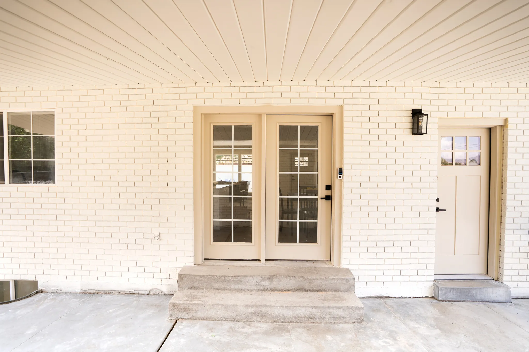 Exterior featuring light-colored brick siding, a window with white grilles, and two entryways