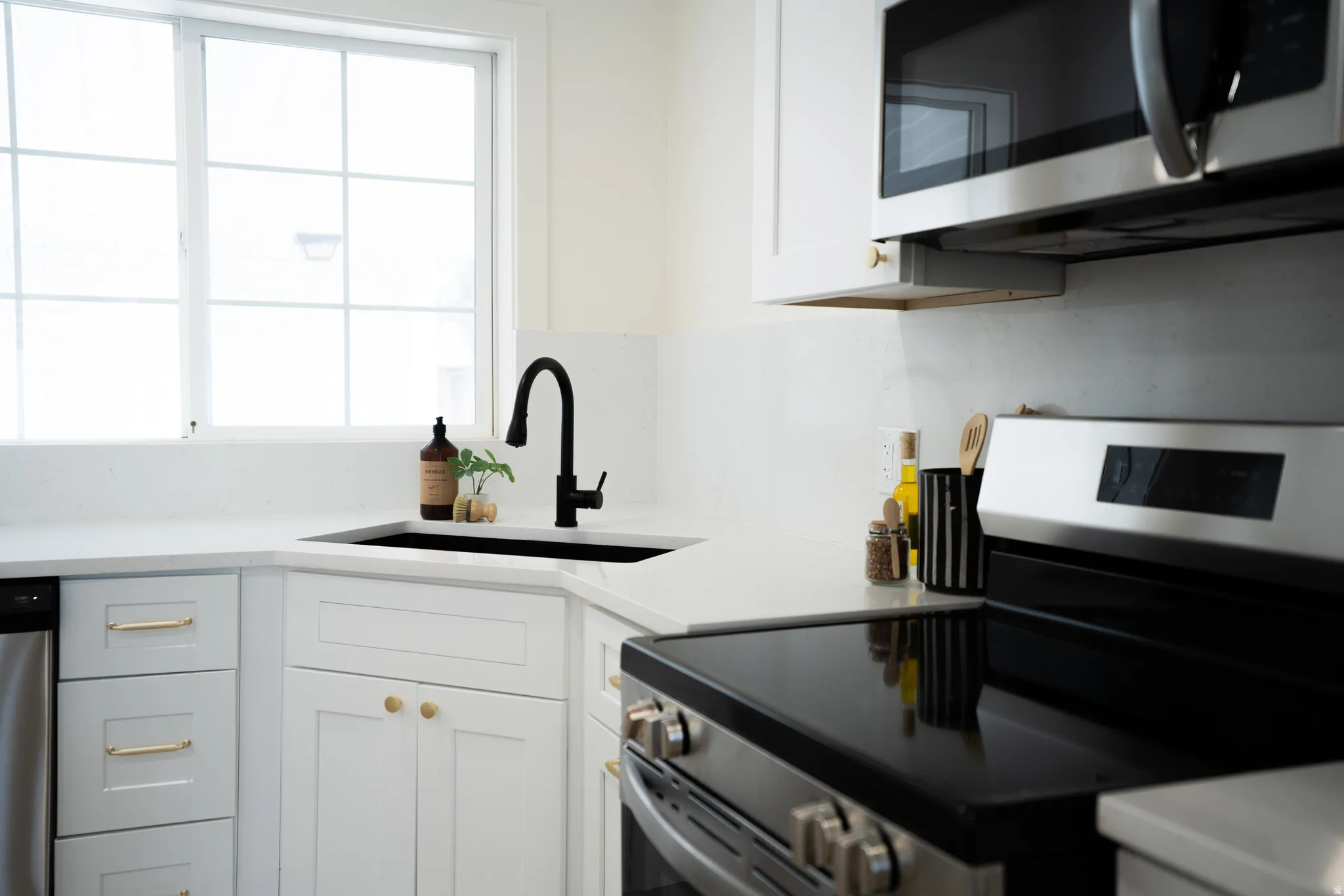 Corner kitchen sink with a matte black faucet, white shaker cabinetry, white countertops, and stainless steel appliances
