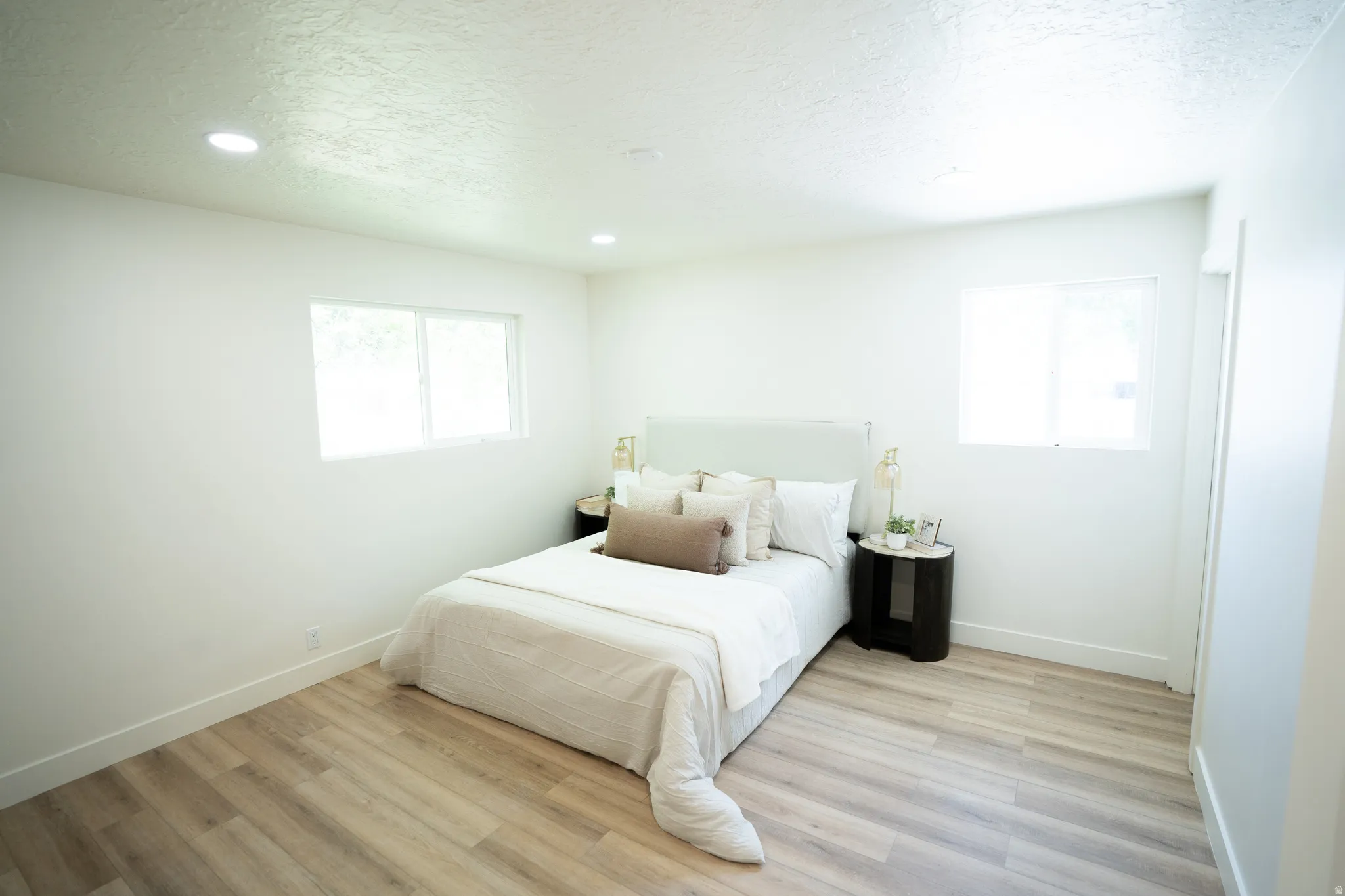 Light-filled room featuring recessed ceiling lighting, two windows, wood-finish flooring, and white baseboards