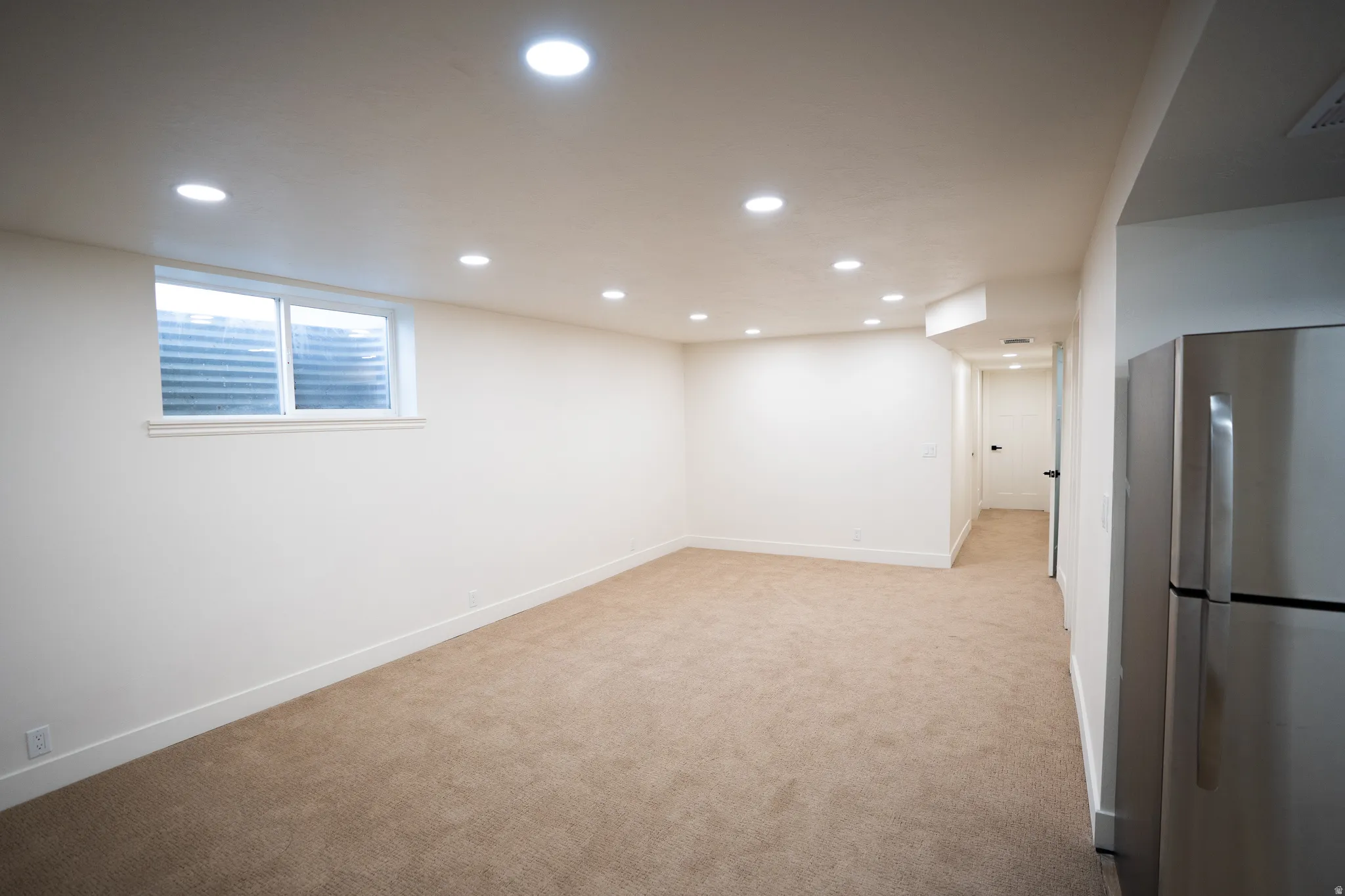 Finished interior space featuring recessed lighting, a window, neutral-toned carpeting, white baseboards, and a stainless steel refrigerator
