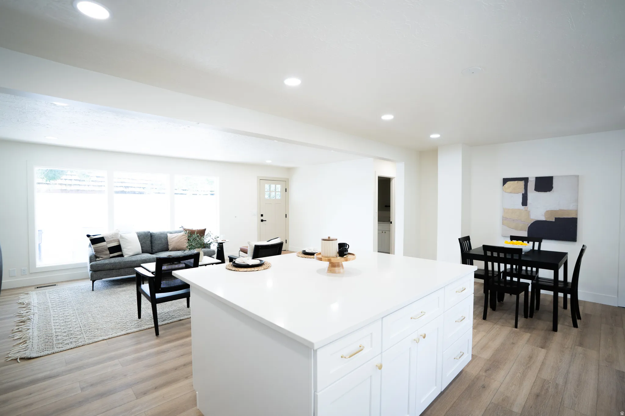 White kitchen island with gold-tone hardware, wood-finish flooring, recessed lighting, and a dining area