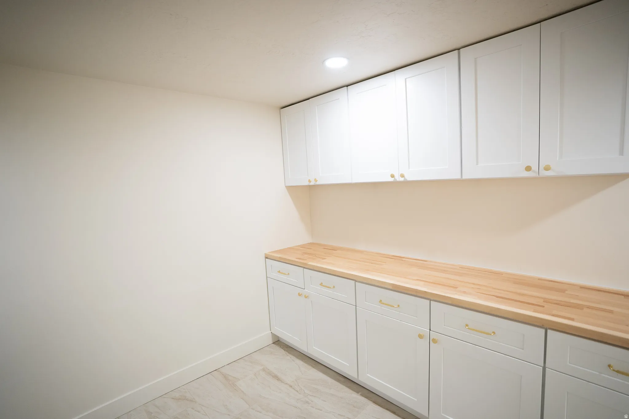 Custom cabinetry featuring white shaker-style doors with gold-tone hardware, wood-finish countertops, and recessed lighting