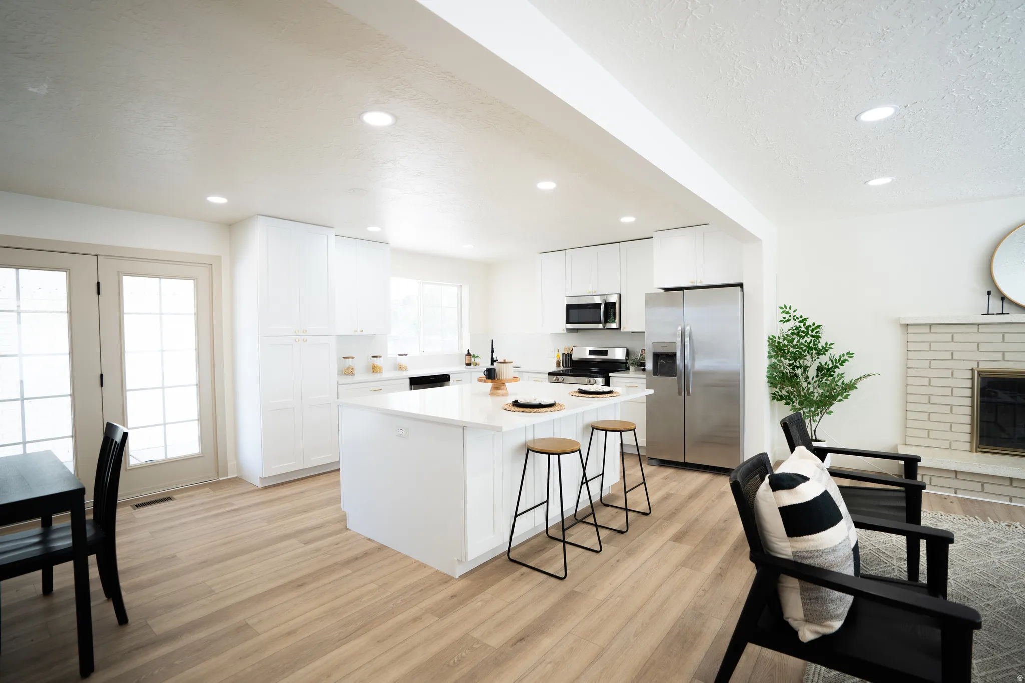 Bright kitchen featuring white cabinetry, a large center island with seating, stainless steel appliances, and a light wood-finish flooring