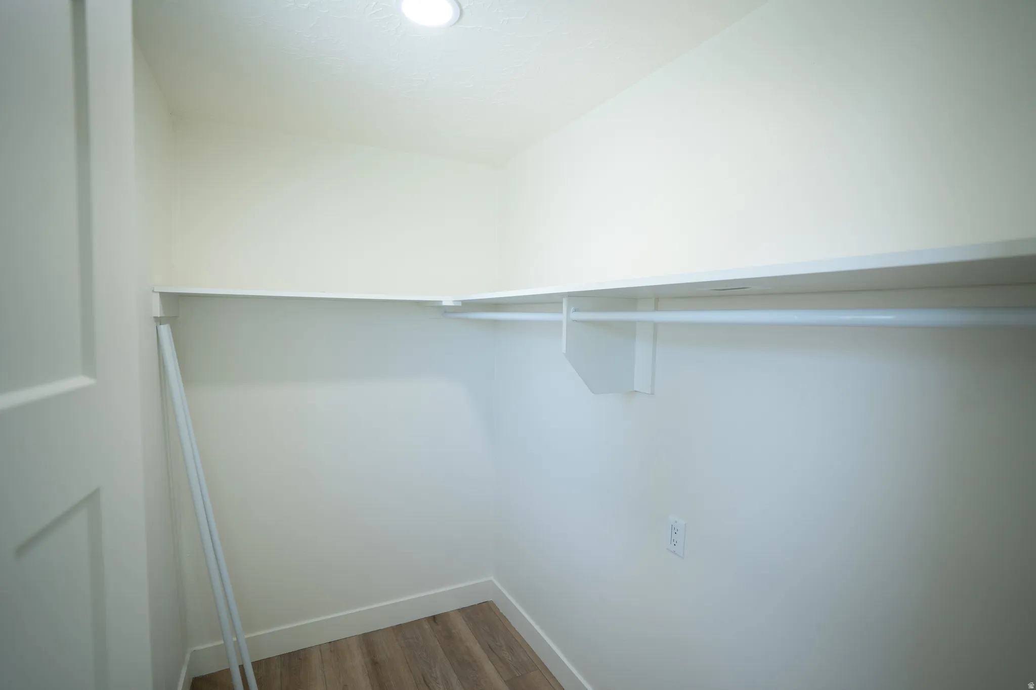 Walk-in closet with L-shaped shelving, clothing rod, recessed lighting, and wood-finish flooring
