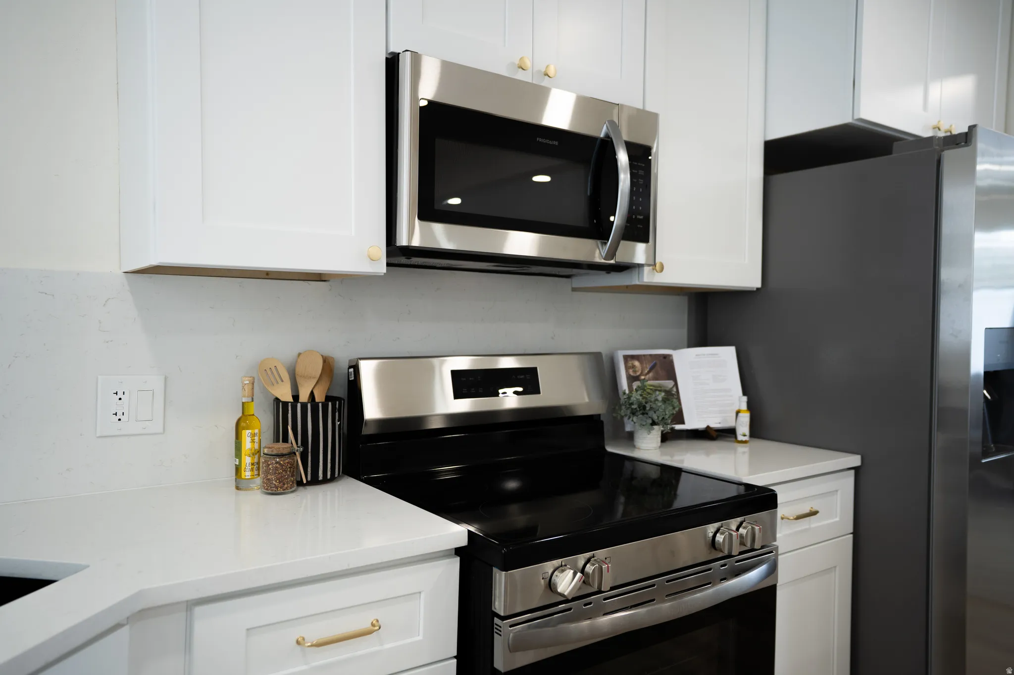 Kitchen featuring white cabinetry, light-toned countertops, and stainless steel appliances including a built-in microwave and range