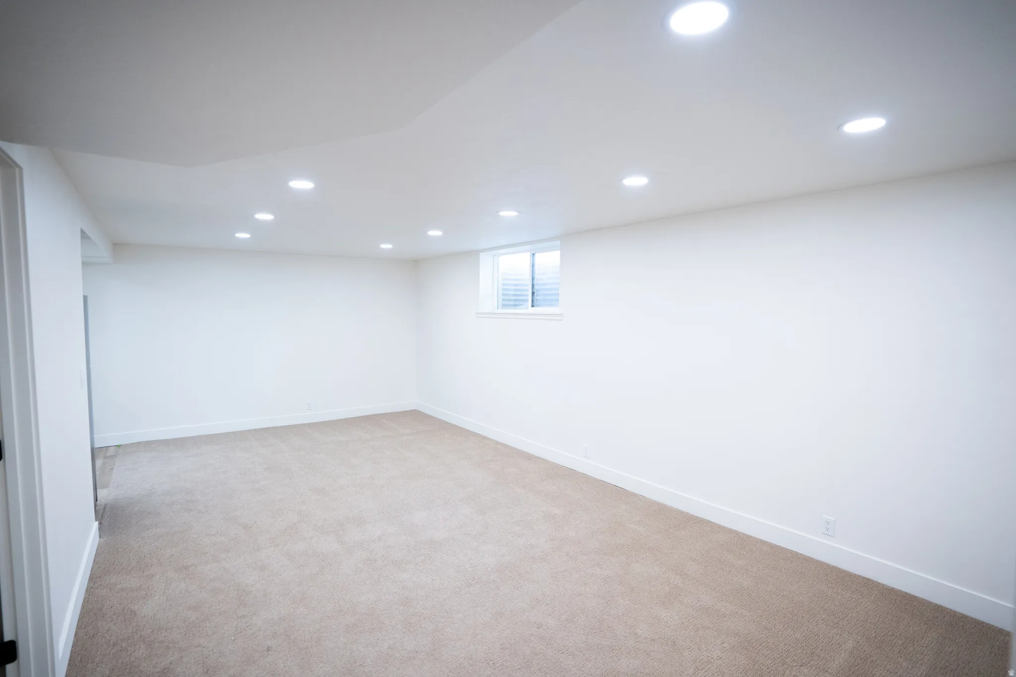 Spacious room featuring neutral carpeting, recessed ceiling lighting, a single window with horizontal blinds, and white baseboards