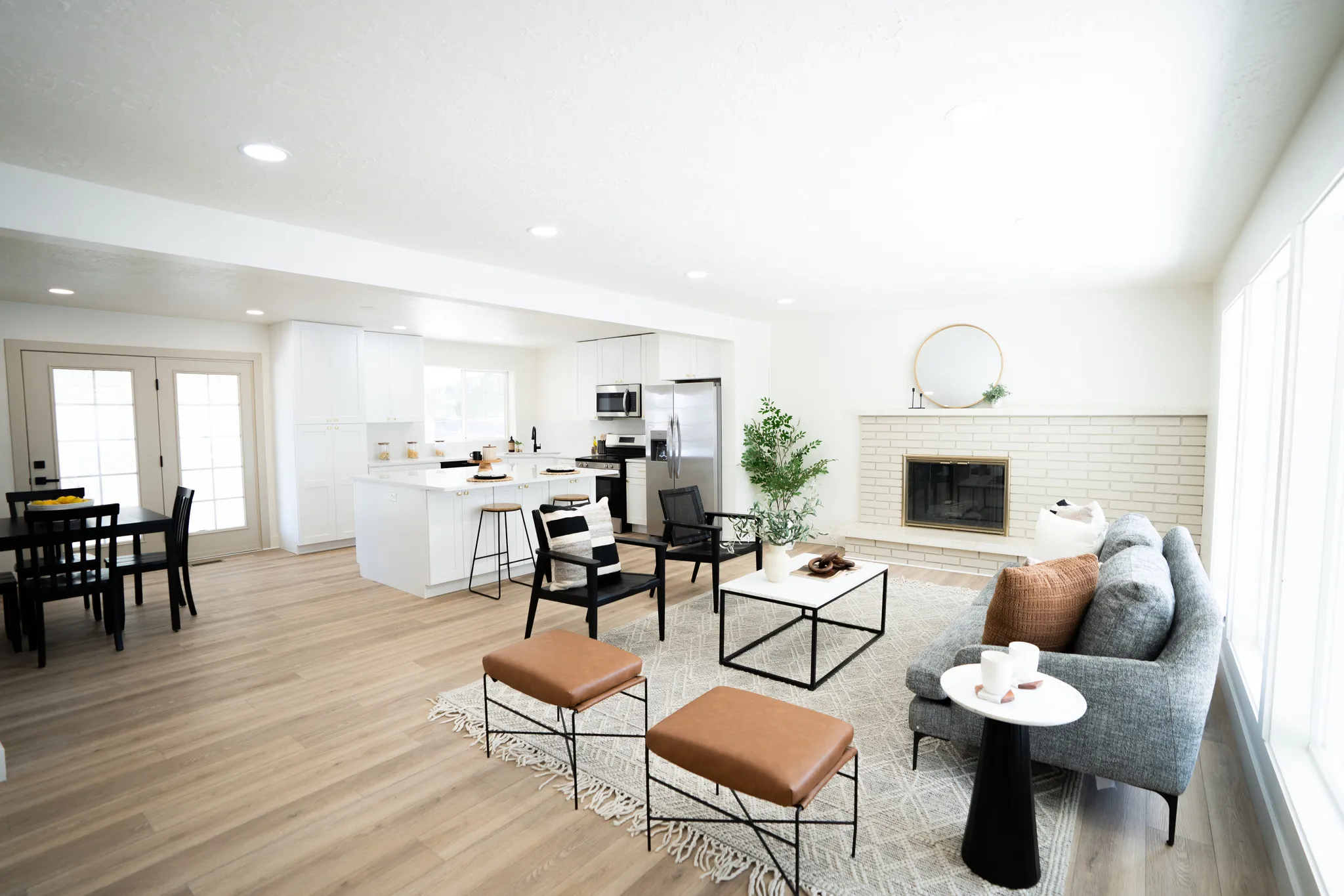 Open-concept living space featuring wood-finish flooring, a white brick fireplace, recessed lighting, and large windows