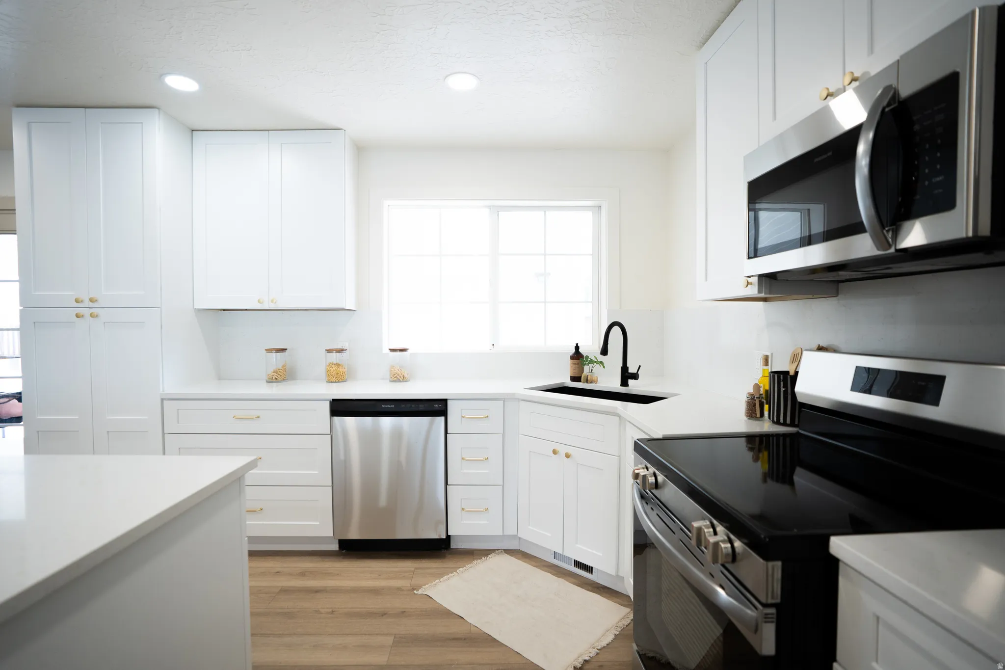 Contemporary kitchen featuring white cabinetry, light-toned countertops, wood-finish flooring, recessed lighting, and stainless steel appliances