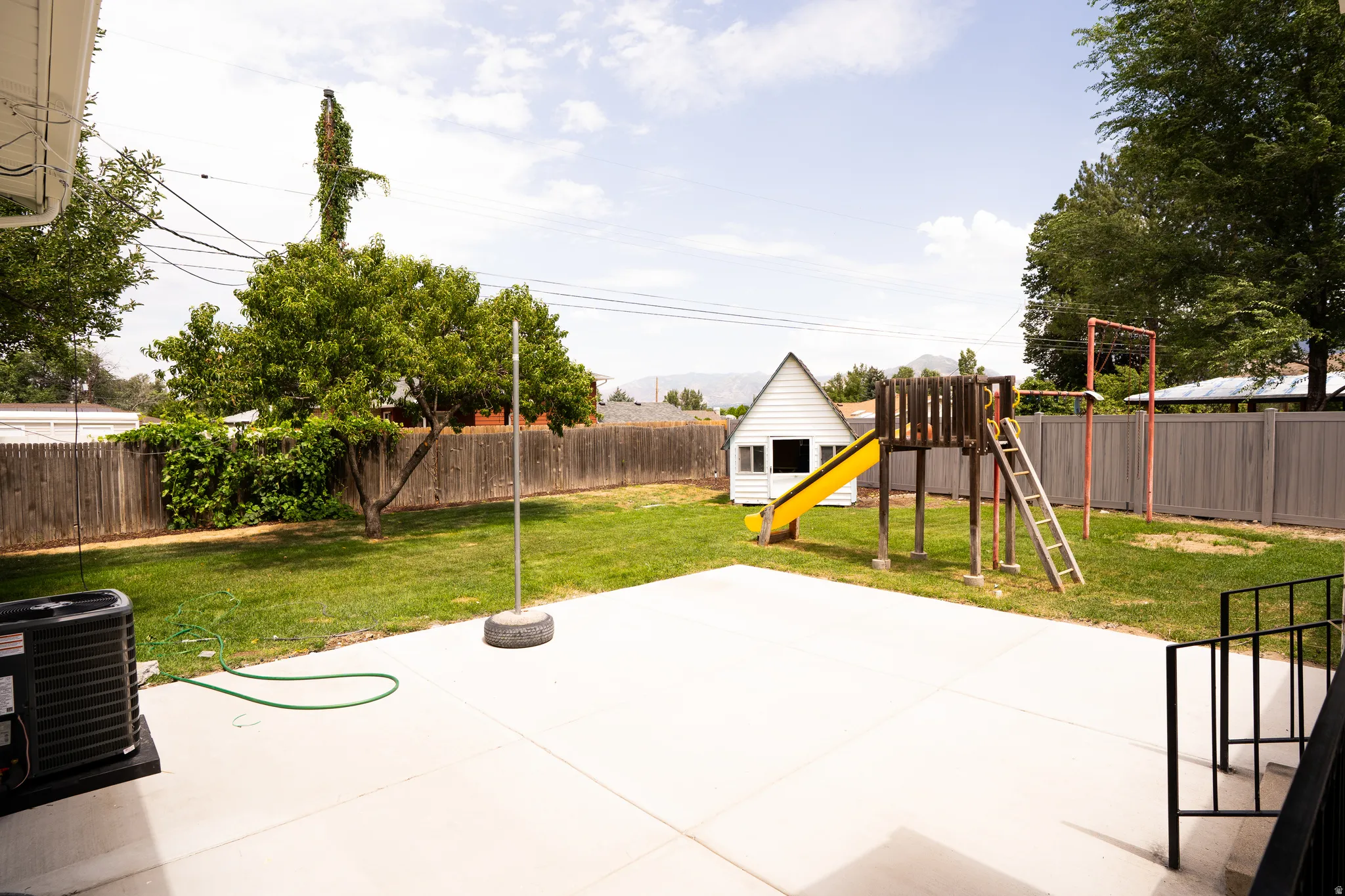 Expansive backyard featuring a large concrete patio, mature trees, and a wooden privacy fence