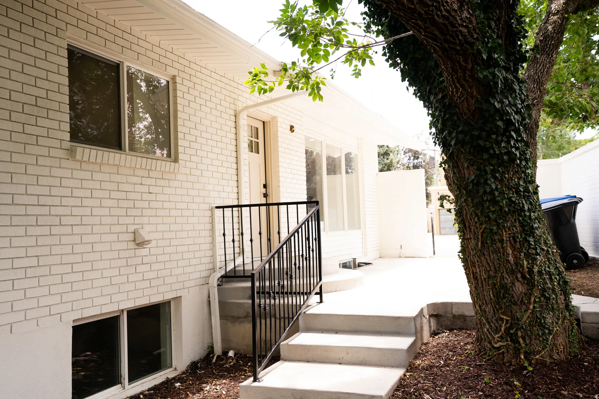 White brick exterior featuring a multi-pane door, a window with a brick sill, and a concrete patio with steps