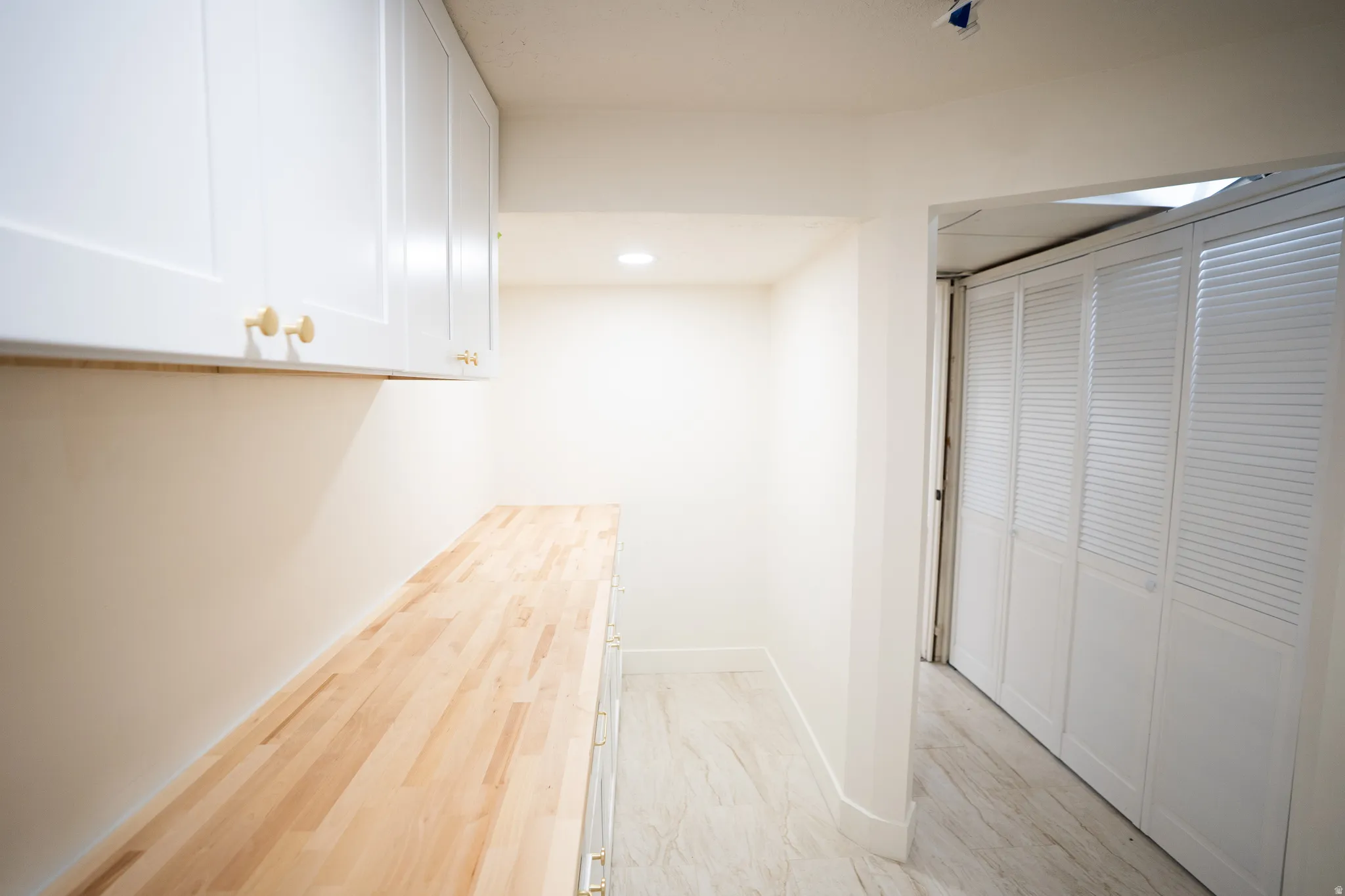 White shaker-style cabinetry with gold-tone hardware, wood-finish countertop, recessed lighting, and light-toned flooring