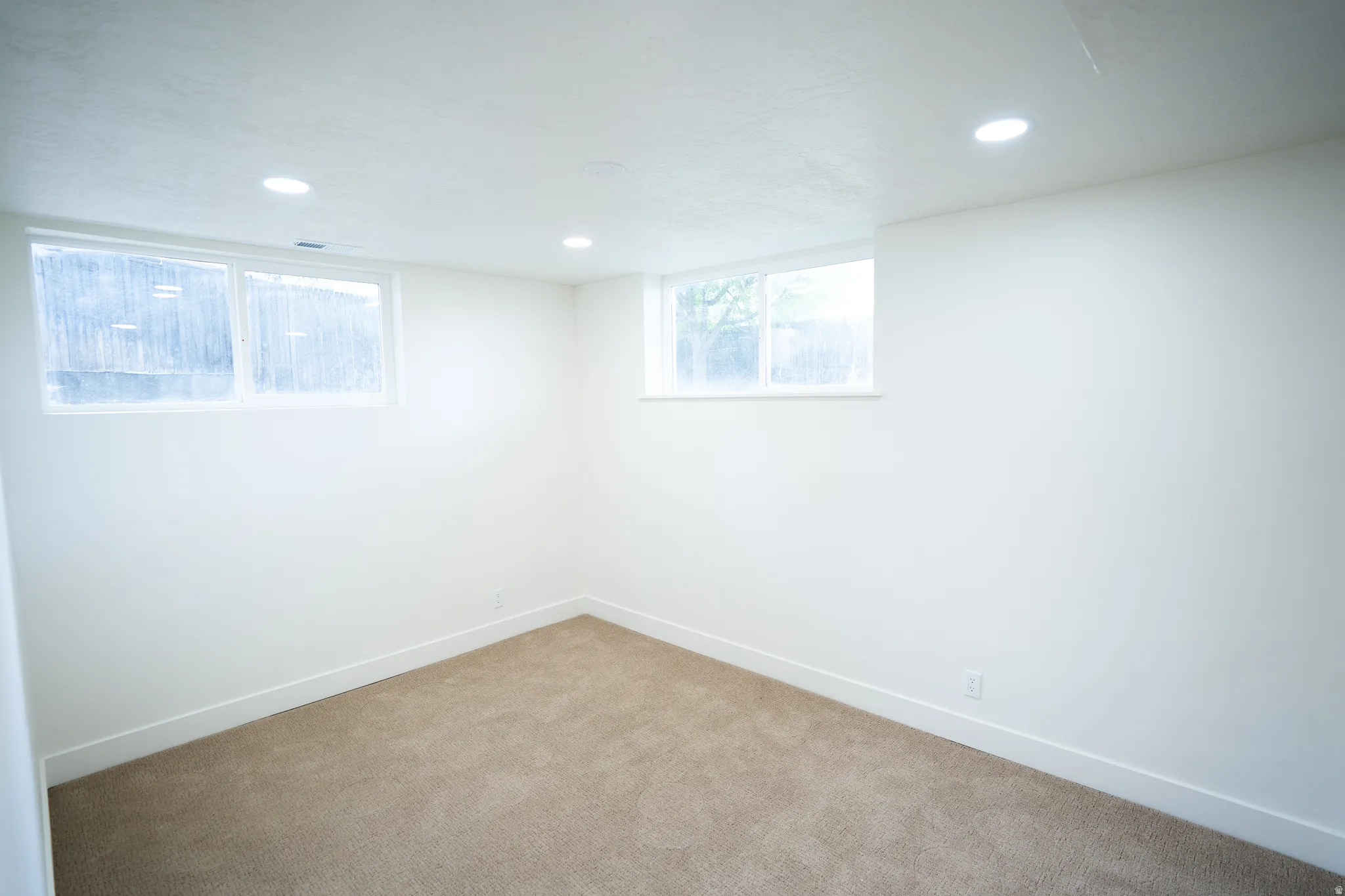 Carpeted room featuring white walls, recessed ceiling lighting, and two windows