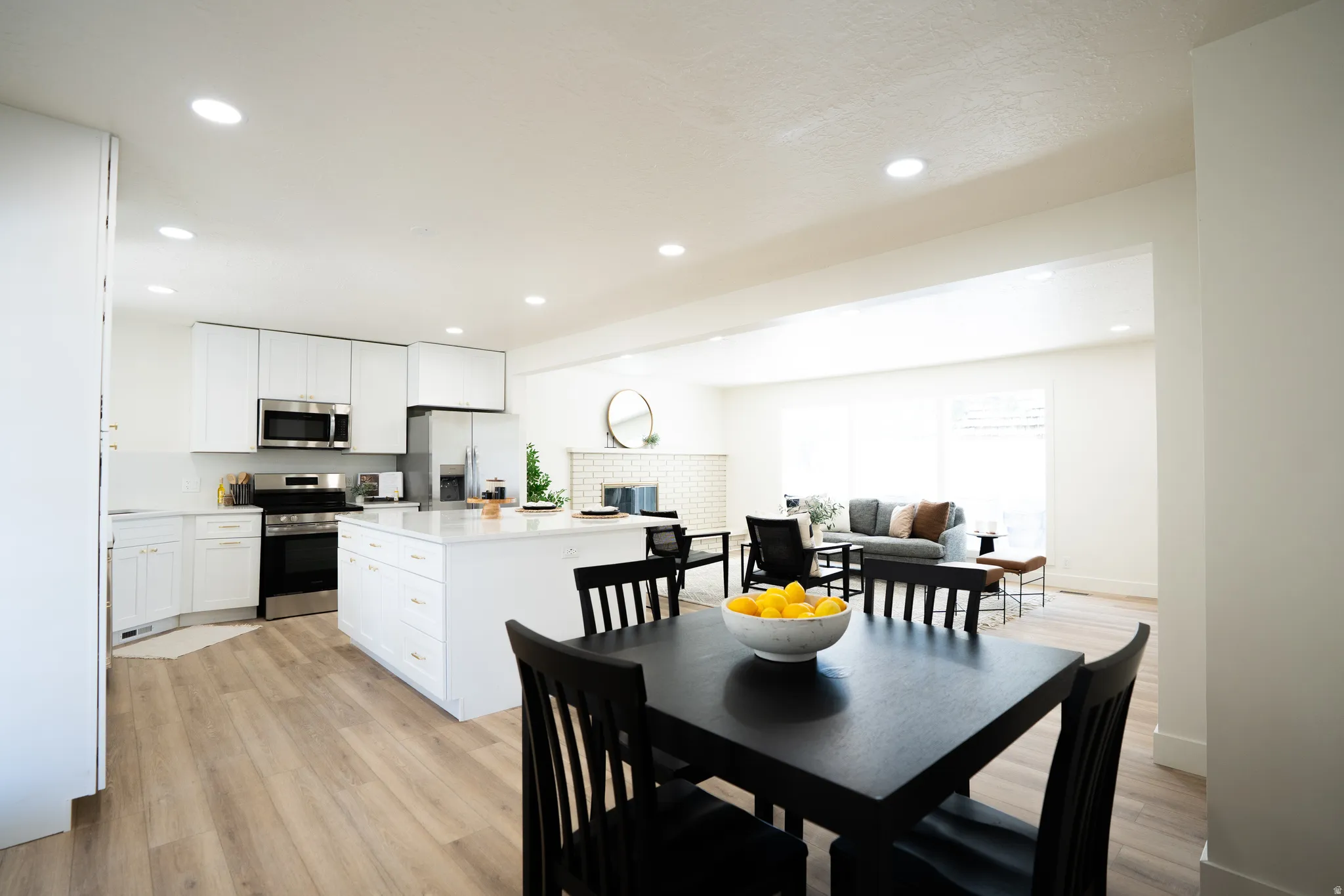 Bright, open-concept kitchen featuring white cabinetry, stainless steel appliances, a center island with countertop seating, and wood-finish flooring