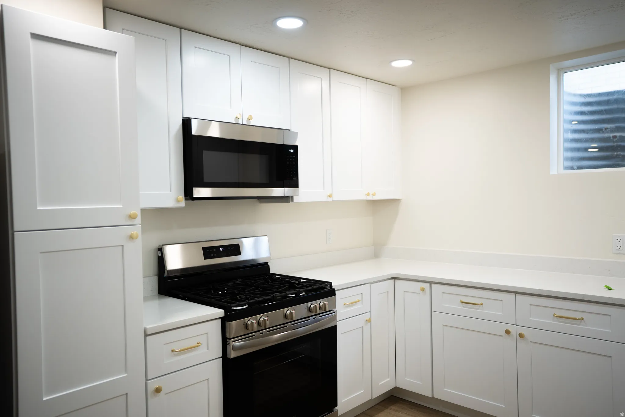 Modern kitchen featuring white shaker-style cabinetry with gold-tone hardware, stainless steel appliances, and light-colored countertops