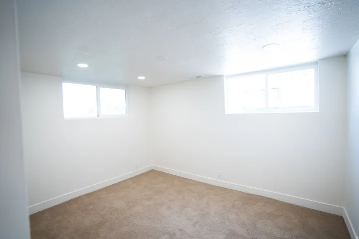 Spacious room featuring neutral carpeting, white baseboards, and two windows