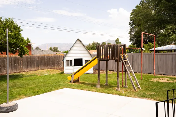 Expansive backyard featuring a concrete patio, mature trees, and a full perimeter fence