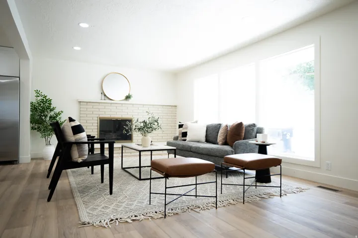 Spacious living area featuring light wood-finish flooring, recessed lighting, and a white brick fireplace with a mantel