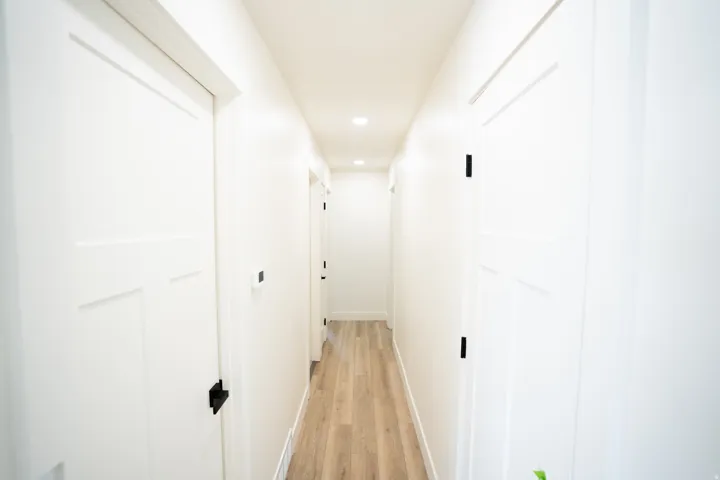 Hallway featuring crisp white walls, wood-finish flooring, recessed lighting, and modern white doors with black hardware