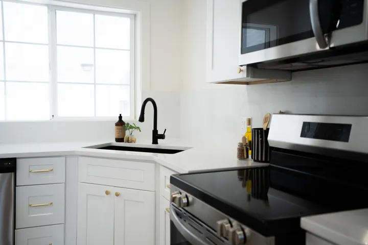 Corner kitchen sink with a matte black faucet, white shaker cabinetry, white countertops, and stainless steel appliances