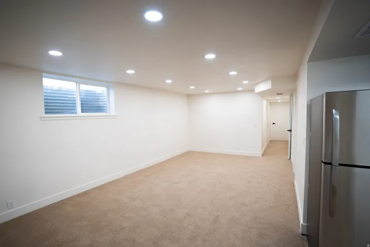 Finished interior space featuring recessed lighting, a window, neutral-toned carpeting, white baseboards, and a stainless steel refrigerator