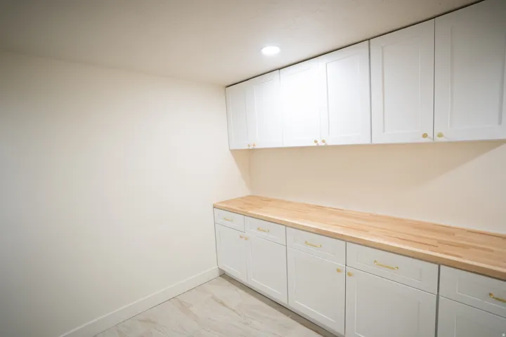 Custom cabinetry featuring white shaker-style doors with gold-tone hardware, wood-finish countertops, and recessed lighting