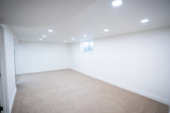 Spacious room featuring neutral carpeting, recessed ceiling lighting, a single window with horizontal blinds, and white baseboards