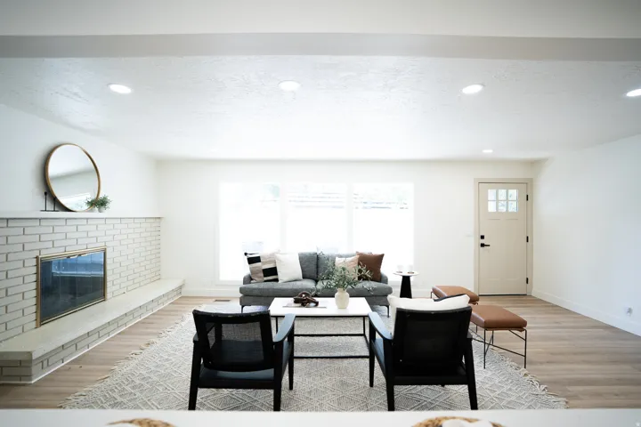 Spacious living area featuring light wood-finish flooring, a white brick fireplace with hearth, recessed lighting, and large windows