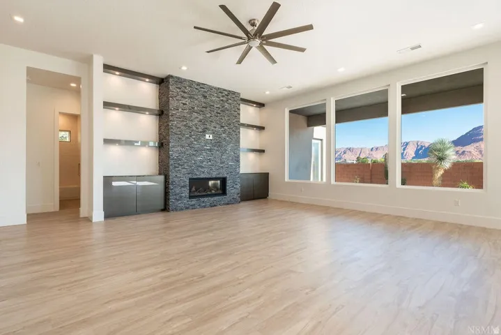 Spacious living area featuring light wood-finish flooring, a stone-clad fireplace, and built-in shelving with integrated lighting