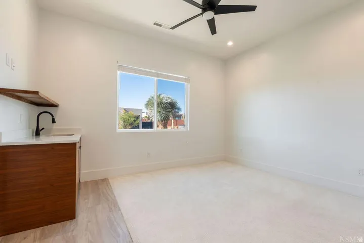 Spacious room featuring a wet bar with wood-finish cabinetry, a large window, recessed lighting, a ceiling fan, and carpeted flooring