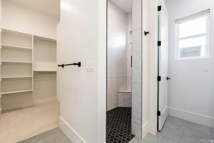 Walk-in closet with built-in shelving, shower with patterned white wall tile and black hexagonal floor tile, and a single window