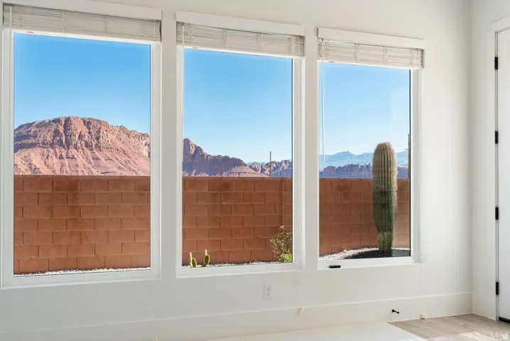 Bright interior space featuring three large windows, white trim, wood-finish flooring, and a desert mountain backdrop