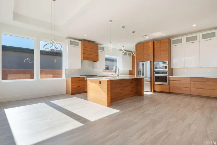 Open-concept kitchen featuring an oversized island, wood-finish cabinetry, stainless steel appliances, and contemporary pendant lighting