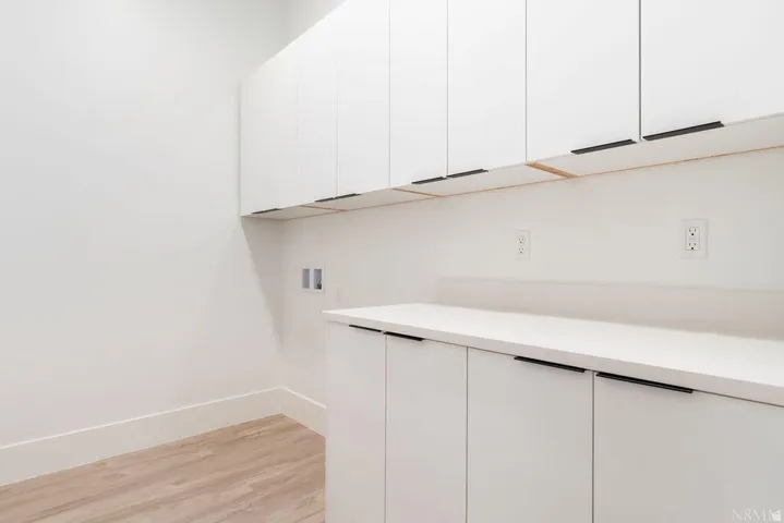 Bright white cabinetry with linear black hardware, light-toned countertop, and wood-finish flooring