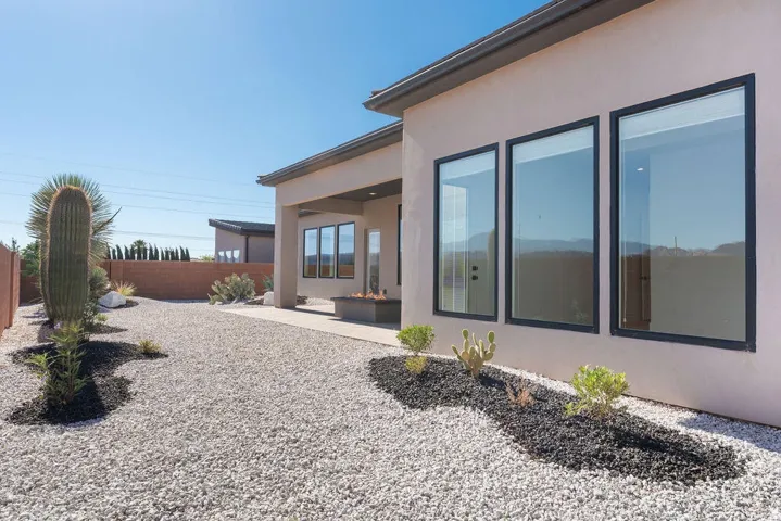 Exterior featuring a covered patio with a built-in fire pit, large windows with dark trim, and a low-maintenance xeriscaped yard