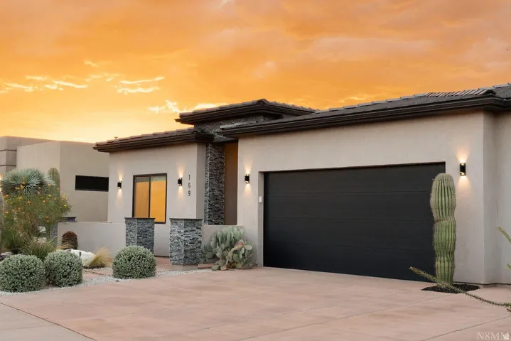 Contemporary exterior with stucco finish and stone accents, featuring a dark garage door, desert landscaping, and modern exterior lighting