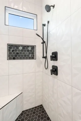 Walk-in shower featuring black hexagon tile flooring, white textured wall tiles, a built-in bench, and a rectangular window