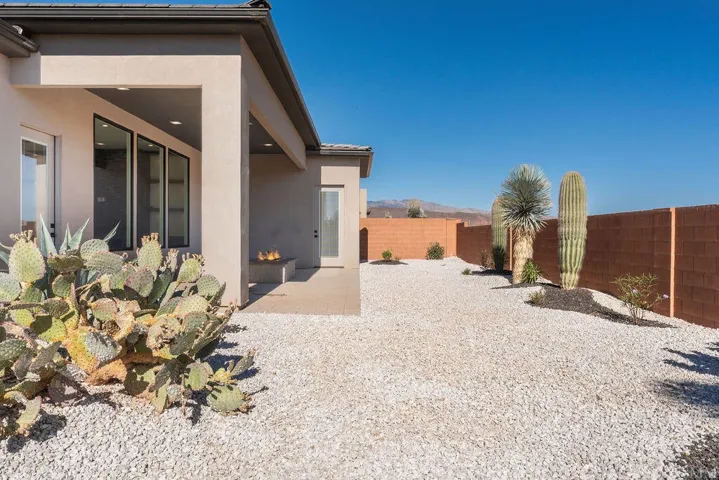 Desert-landscaped backyard featuring gravel ground cover, mature cacti, an integrated fire pit, a covered patio area, and a privacy wall