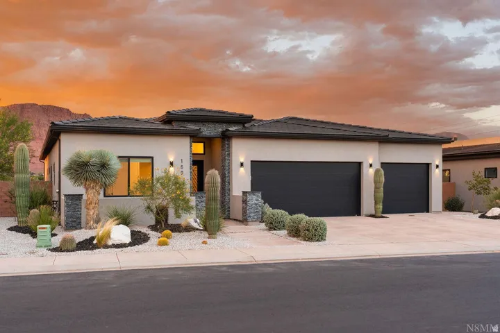 Contemporary stucco exterior featuring stone accents, a dual garage, desert landscaping, and a concrete driveway