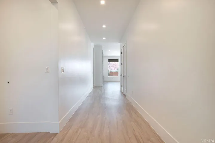 Corridor featuring light wood-finish flooring, recessed lighting, white baseboards, and white walls