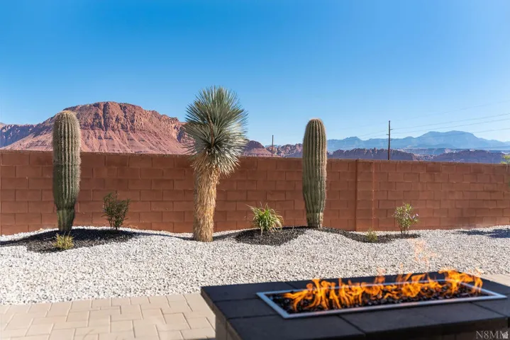 Outdoor patio featuring a built-in fire pit with a rectangular burner, paver flooring, and a low maintenance landscaping with cacti and gravel