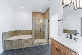 Bathroom featuring hexagonal floor tiling, a built-in soaking tub with tile surround, a glass-enclosed shower, a vanity with an integrated sink and matte black fixtures, and a decorative ceiling light fixture