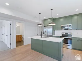 Modern kitchen featuring sage green cabinetry, stainless steel appliances, a center island with sink and seating, and wood-finish flooring