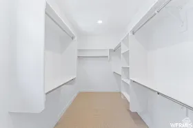 Walk-in closet featuring light-colored flooring, white walls, built-in shelving, and multiple hanging rods