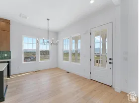 Bright interior space featuring wood-finish flooring, a contemporary chandelier, multiple windows with grid patterns, and a full-light glass panel door