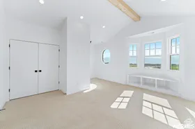 Spacious room featuring a vaulted ceiling with exposed wood beam, a bay window with integrated shelving, and a circular window