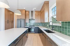 Gourmet kitchen featuring a large central island with a white countertop, two-tone cabinetry, stainless steel appliances, a range hood, and green tile backsplash